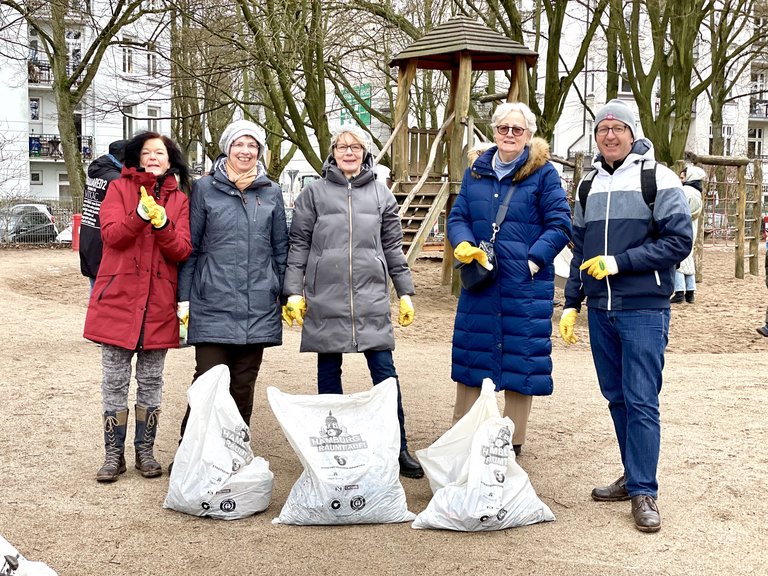 Fünf Menschen stehen mit gefüllten Müllbeuteln auf dem Schinkelplatz in Hamburg-Winterhude